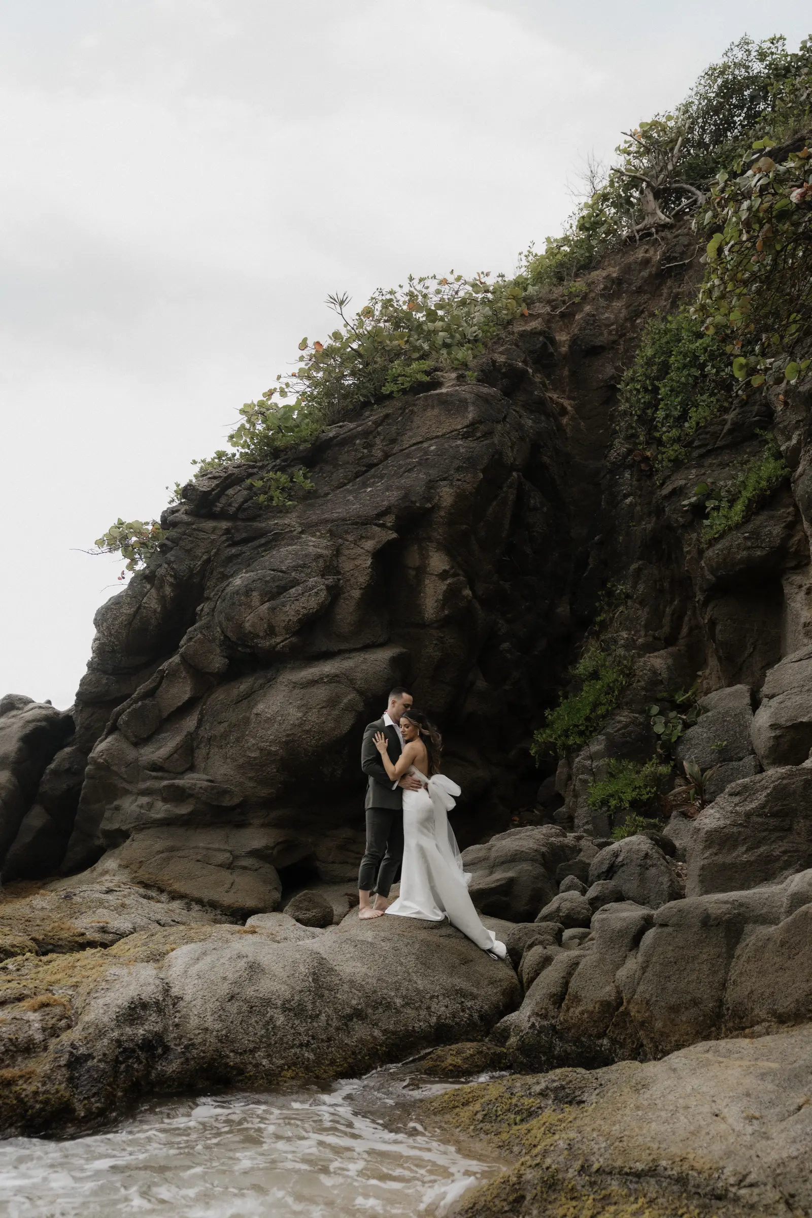 Bride and groom embracing on a rocky Puerto Rico coastline with the ocean behind them