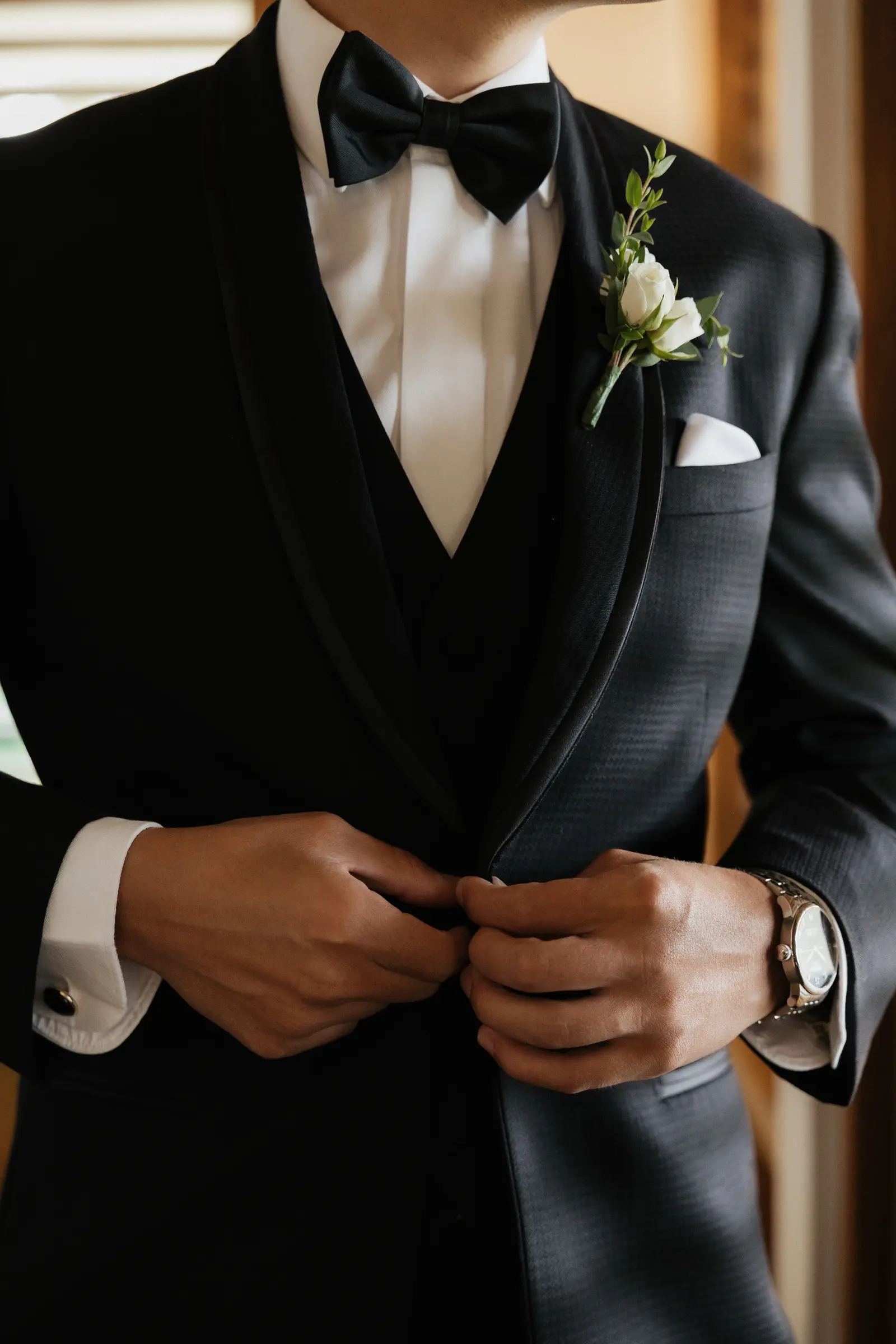 Groom buttoning his tuxedo jacket, boutonniere detail