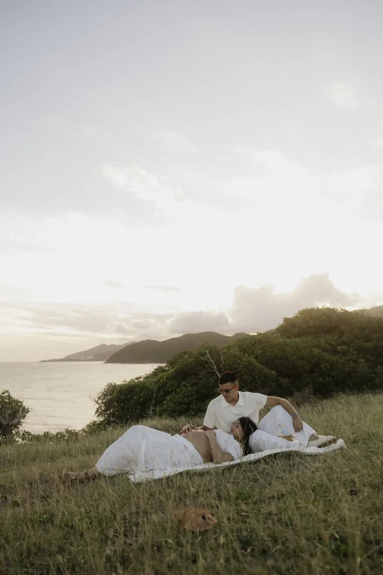 Couple lying together in a grassy field overlooking the coast