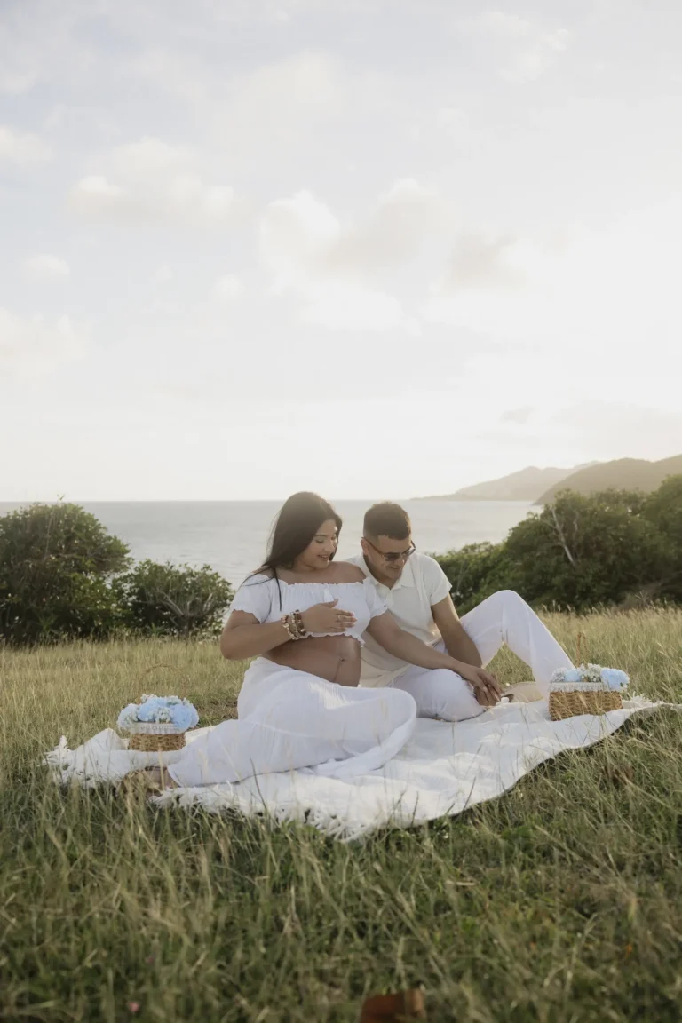 Pregnant couple sitting together in a grassy field at golden hour