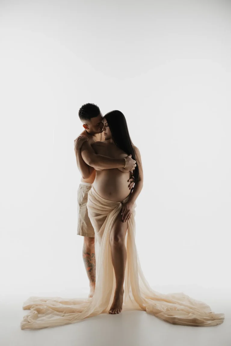Couple embracing in flowing beige fabric, studio portrait