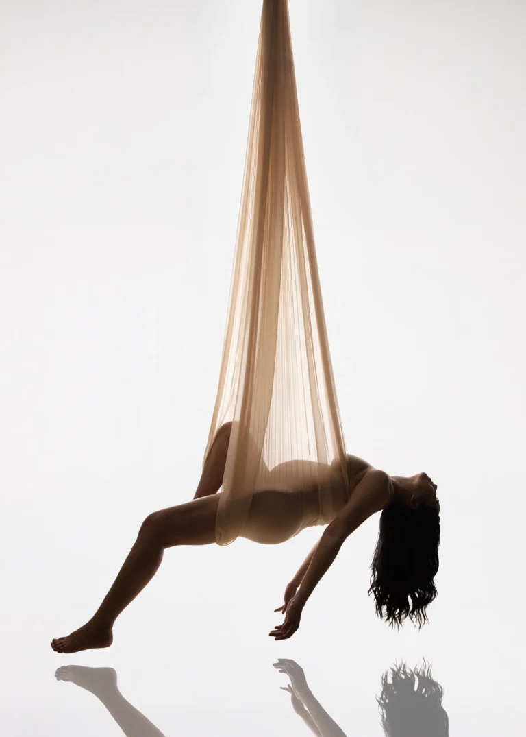 Pregnant woman suspended in a fabric hammock sling, studio portrait