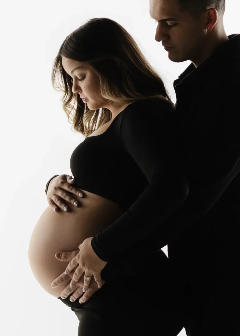 Couple in a dark studio setting, close-up of hands resting on the pregnant belly