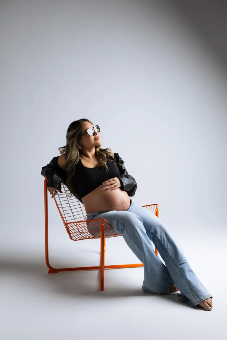 Pregnant woman seated in a modern wire chair wearing denim and a black top