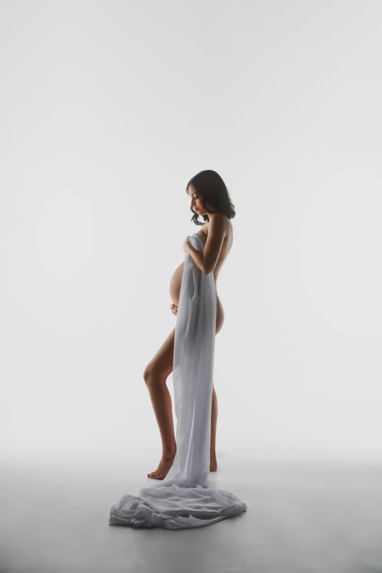 Pregnant woman in a white gown with a flowing train, studio portrait