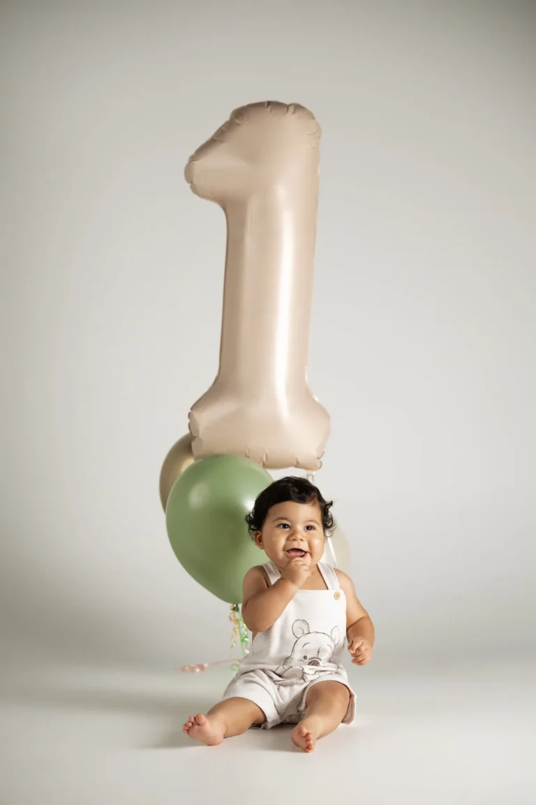 Baby celebrating a first birthday with balloon numbers in a neutral studio setting