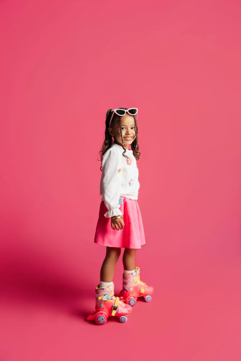 Child in roller skates and heart-shaped sunglasses standing against a pink studio backdrop