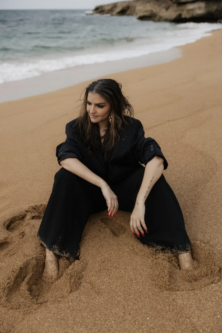 Woman in a black outfit seated on the sand at the beach