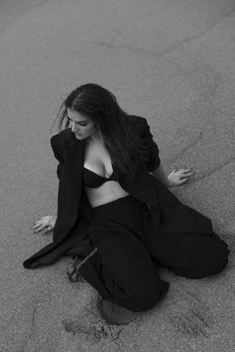 Black-and-white artistic portrait of a woman kneeling on textured sand