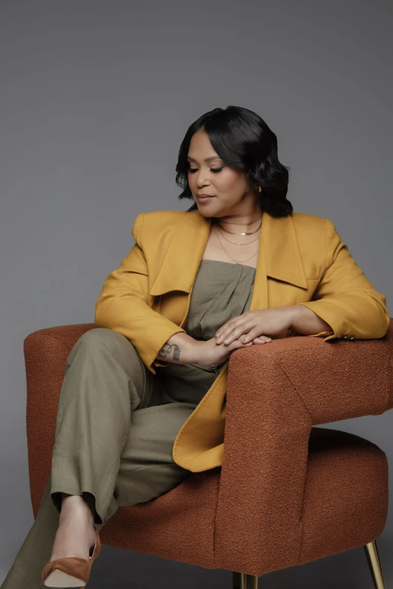 Woman in a mustard blazer seated in an orange armchair for an editorial portrait