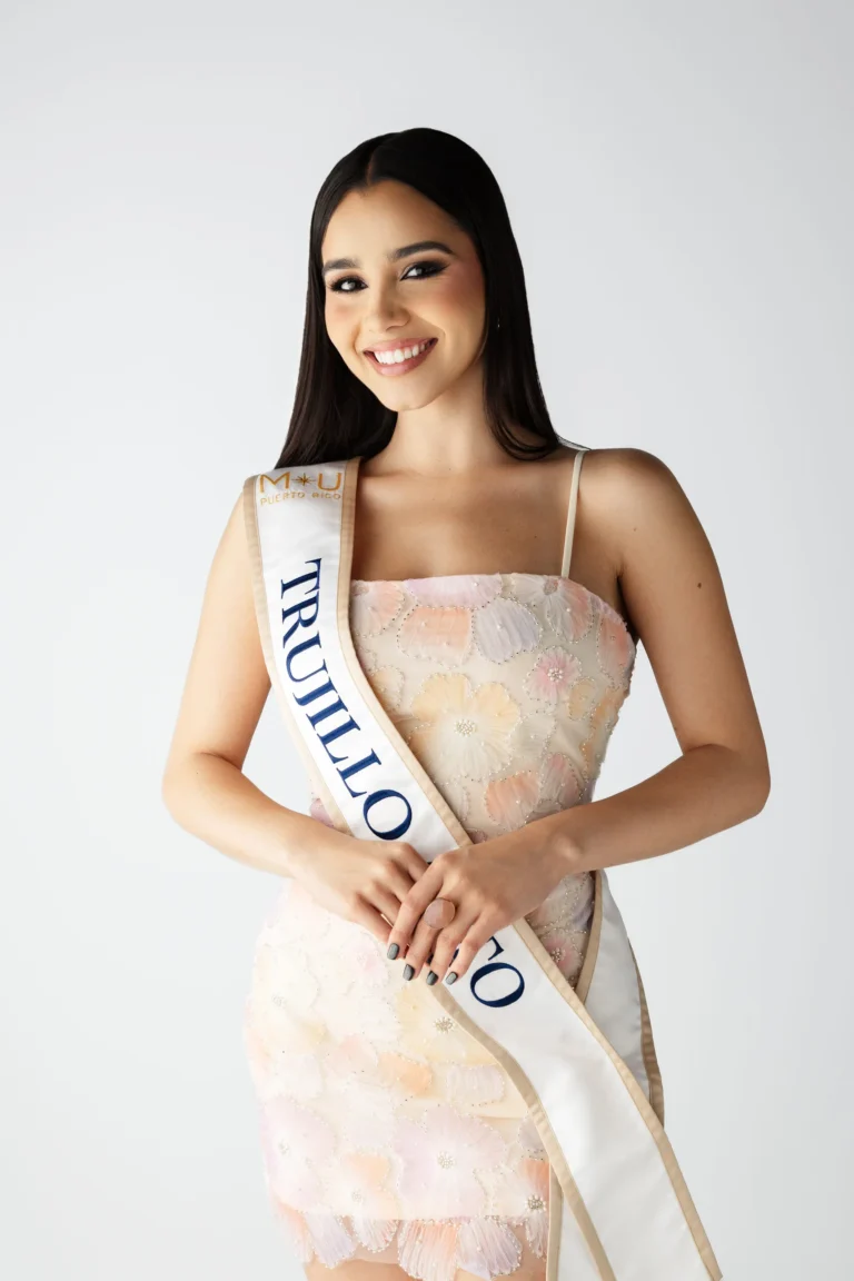 Woman wearing a pageant sash and floral dress, smiling for a studio portrait