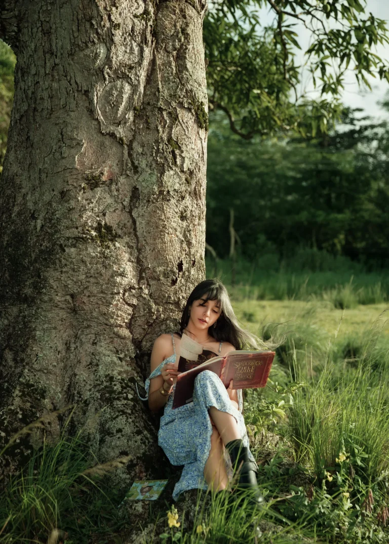 Woman reading a book while seated under a tree outdoors