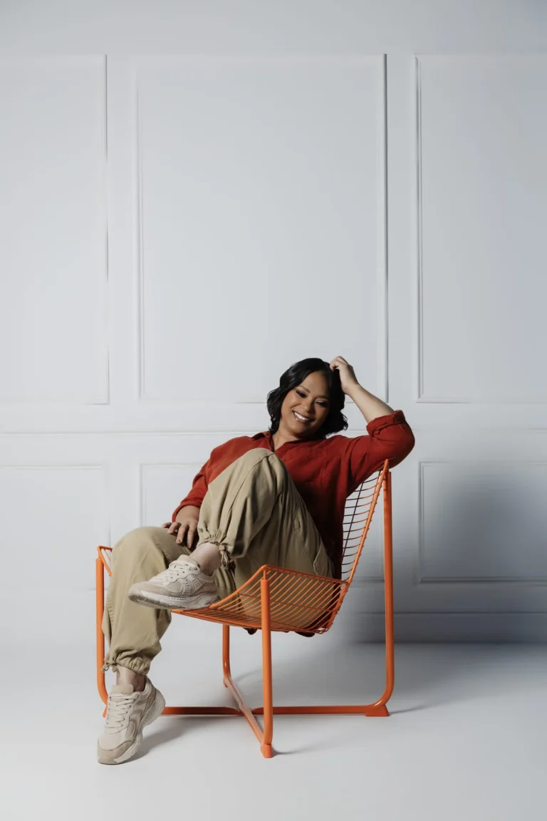 Woman in a red sweater and cream pants seated in an orange chair