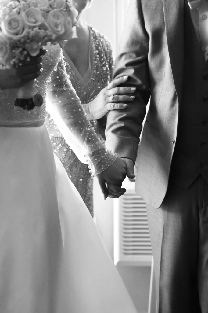 Couple kissing beneath a wooden wedding pavilion with a lit chandelier overhead, black and white